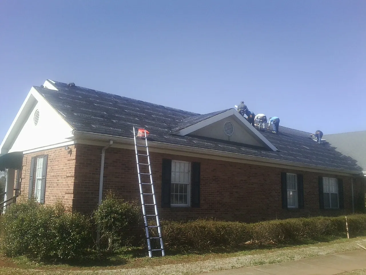 Crew tearing shingles off a brick ranch roof with a ladder set — Emergency Roof Repair work by our crew in Humarock