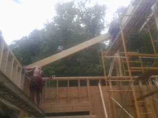Carpenter raising a rafter beam on a new second story frame in Humarock