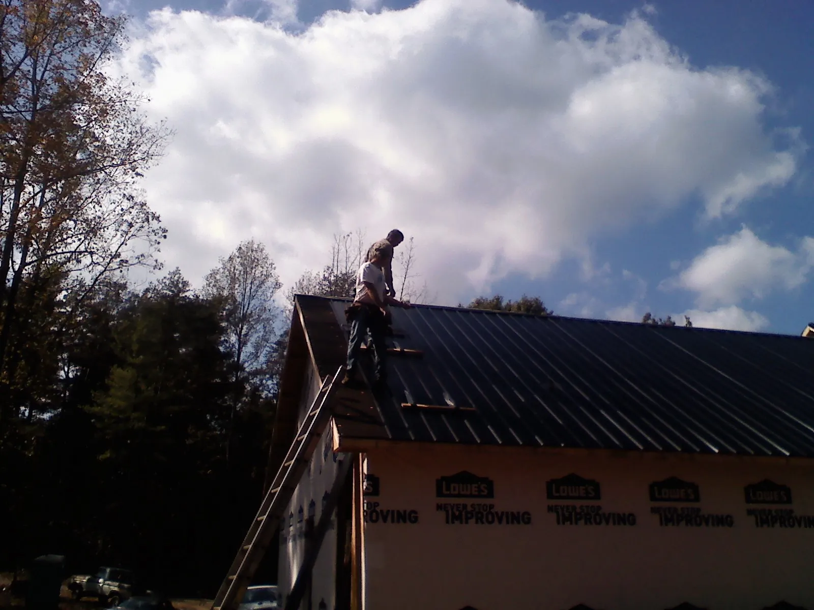Roofer fastening dark metal panels high against a cloudy sky, from a Roof Inspection job in Humarock